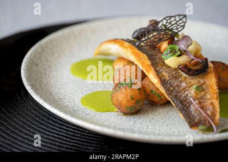 Gebratenes Branzino-Fischfilet mit marinierten Pilzen, Spargelsauce und Butterkartoffeln auf einem Teller. Selektiver Fokus. Gourmetessen. Stockfoto