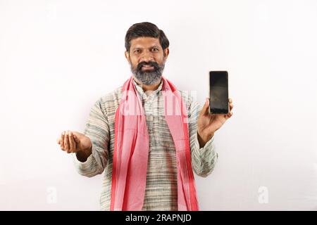 Fröhlicher Landwirt, der den Bildschirm des Mobiltelefons zeigt und Technologie verwendet. Samen in der anderen Hand. Glücklicher indischer bärtiger Bauer im ländlichen Indien Konzept. Stockfoto