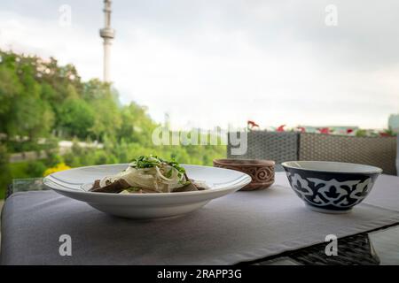 Zusammensetzung des leckeren kasachischen Nationalgerichts beshbarmak auf einem Teller mit Azy, Mehltortillas, Zwiebeln Stockfoto