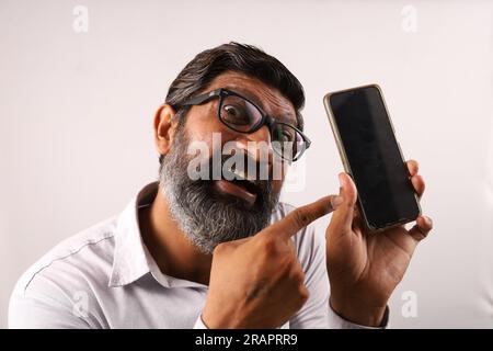 Mittelalter, bärtiger Indianer, der ein Hemd in der Hand hält und ein Handy in der Hand zeigt. Flippige Ausdrücke auf einem Ebenen Hintergrund. Stockfoto