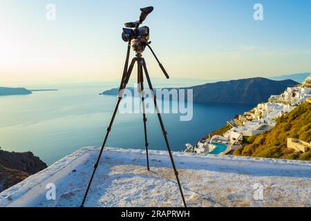 Stativ auf Aussichtsplattform, das auf den Sonnenuntergang wartet. Foto gemacht im Dorf Imerovigli, Santorin, Griechenland. Am Abend gibt es herrliche Sonnenuntergänge Stockfoto