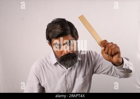 Porträt eines bärtigen Indianers, der im Zorn ein Hemd trägt und ein Lineal in der Hand hält. Seltsame Ausdrücke eines Psycholehrers. Betäubt öffnete sich wütende Augen. Stockfoto
