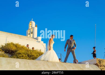 Frisch verheiratete Paare, die auf dem Dach des Höhlenhauses auf den Klippen in Fira, der Hauptstadt Santorins, eine Fotosession machen – ein beliebtes Hochzeitsziel Stockfoto