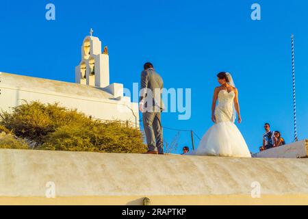 Frisch verheiratete Paare, die auf dem Dach des Höhlenhauses auf den Klippen in Fira, der Hauptstadt Santorins, eine Fotosession machen – ein beliebtes Hochzeitsziel Stockfoto