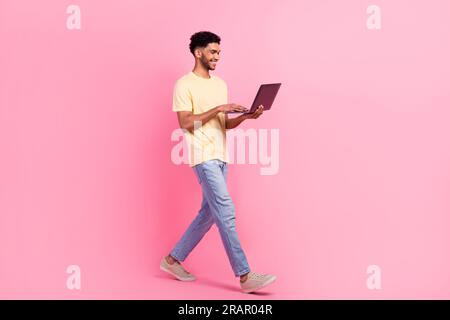 Ganzkörperkadre des Spaziergangs mit einem Netbook junger Mann, der Content-Plan-Programmmanagement verfasst, isoliert auf pinkfarbenem Hintergrund Stockfoto