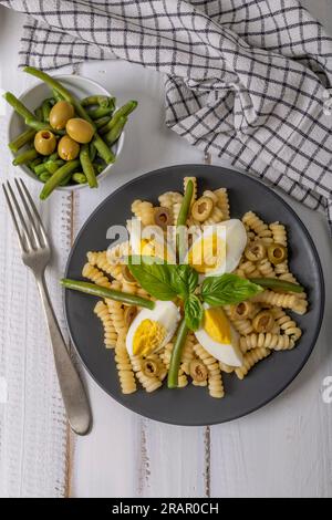 Ein Teller mit kalter Pasta mit gekochten Eiern, gekochten grünen Bohnen, Oliven und Basilikumblättern Stockfoto