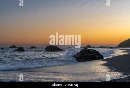 Am Strand entlang der Küste Oregons spritzt Wasser von einem Felsen bei Sonnenuntergang Stockfoto