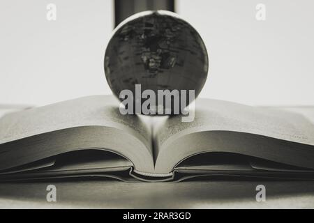 Globe befindet sich im Zentrum eines offenen Buches, des Konzepts der „Untersuchung des universellen Rechts“, eines Schwarzweißbildes. Stockfoto