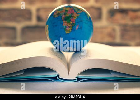 Das Hardcover-Buch ist auf einem Schreibtisch offen, der Globus befindet sich in der Mitte, das Konzept „Lesen ist wie Reisen“. Stockfoto