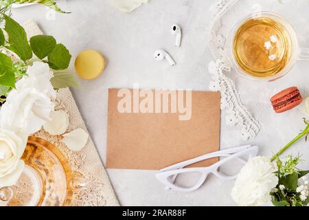 Ästhetisches, feminines Flachbett mit kunstvoll gefertigten Papierumschlägen für Grußworte, Text in weißen Blumen, Gläser, Tee, Makronen und Ohrhörer. Speicherplatz kopieren. Stockfoto