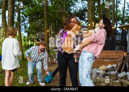 Lustiger Familienmoment mit dem Vater, der einen Gartenbläser benutzt, um seine Frau und seine Tochter zu ärgern, die Hunde halten Stockfoto