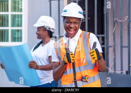 Glücklicher afrikanischer Ingenieur, der einen Schutzhelm und eine reflektierende Jacke mit beiden Daumen nach oben trägt, was ein positives Zeichen der Anerkennung gibt, Daumen nach oben Geste Stockfoto