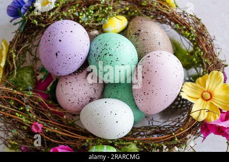 Frohes Osterkonzept. Vorbereitung auf den Urlaub. Farbenfroh dekorierte ostereier in einem Nest mit Blumen Stockfoto