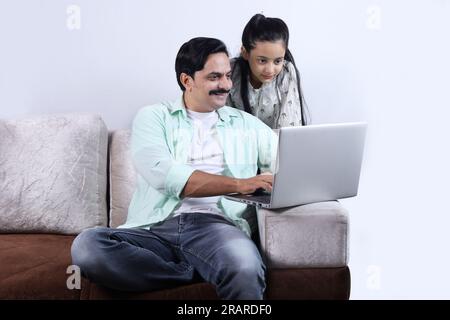 Glückliche indische Familie mit alleinerziehendem Vater und Tochter, die mit einem Laptop surfen und eine angenehme Zeit zusammen verbringen. Die Familie schaut sich das Notebook an. Stockfoto