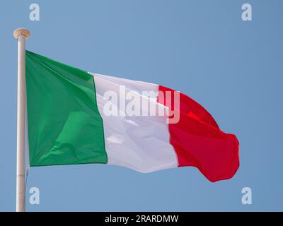 Italien die italienische Nationalflagge, die im Wind auf einem Fahnenmast mit blauem Hintergrund winkt. Stockfoto