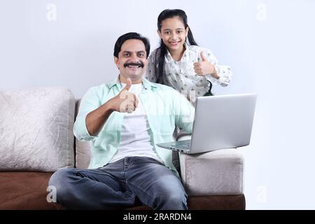 Glückliche indische Familie mit alleinerziehendem Vater und Tochter, die mit einem Laptop surfen und eine angenehme Zeit zusammen verbringen. Die Familie schaut sich das Notebook an. Stockfoto