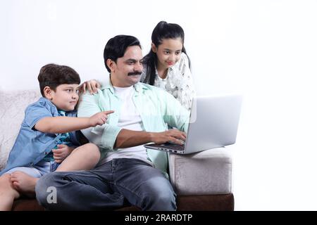 Glückliche indische Familie von Vater, Sohn und Tochter, die mit dem Laptop surfen und eine schöne Zeit zusammen verbringen. Die Familie schaut sich das Notebook an. Stockfoto