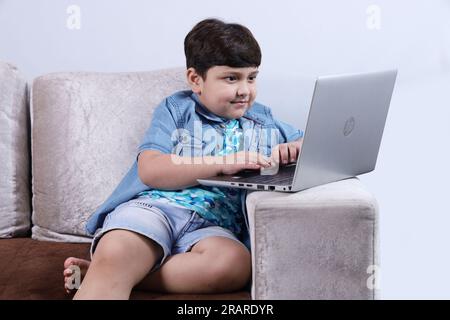Ein glückliches indisches Kind, das mit dem Laptop surft und freudig eine schöne Zeit zusammen hat. Das Kind surft im Internet und schaut in den Laptop. Stockfoto