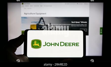 Person, die ein Mobiltelefon mit dem Logo des amerikanischen Unternehmens Deere and Company (John Deere) auf dem Bildschirm vor der Webseite hält. Konzentrieren Sie sich auf das Display des Telefons. Stockfoto
