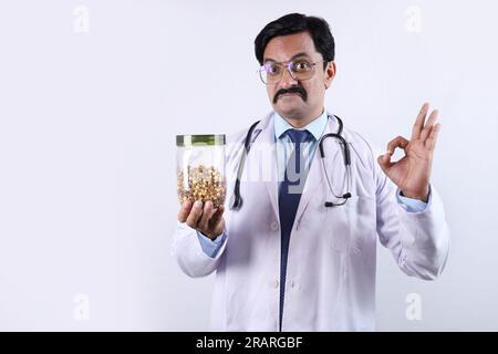 Indischer selbstbewusster Doktor hält ein Glas in der Hand und schlägt vor, frisch und gesund zu essen. Der Arzt steht auf weißem Hintergrund. Stockfoto
