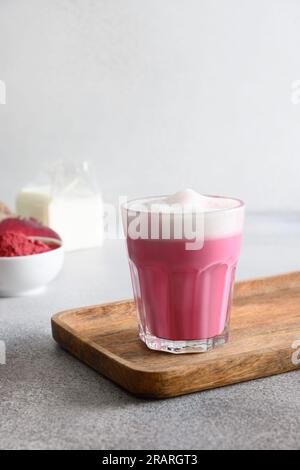 Rote-Bete-Latte aus Rüben-Pulver in Glas, serviert auf einer Holzschale. Trendiges, gesundes veganes und koffeinfreies Getränk. Vertikales Format. Stockfoto