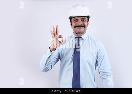 Glücklicher indischer Bauarbeiter, der Ingenieurkonzepte für eine bessere Zukunft macht. Der fröhliche Ingenieur trägt einen Technikhelm und zeigt ein Handy Stockfoto