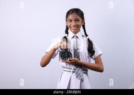 Junge Teenagerin, die einen Wecker in der Hand hält und auf den Wecker zeigt. Stockfoto