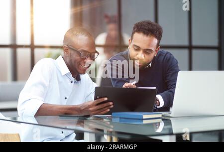 Kollegen, die an einem Tisch in einem modernen Büro sitzen und mit einem Laptop sprechen Stockfoto