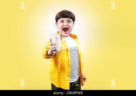 Das Porträt eines aufmerksamen Jungen, das ein Glas Milch in der Hand hält, und das sehr selbstbewusst und mit einem kleinen Champion, gibt ein sehr unartiges und selbstbewusstes Lächeln. Stockfoto