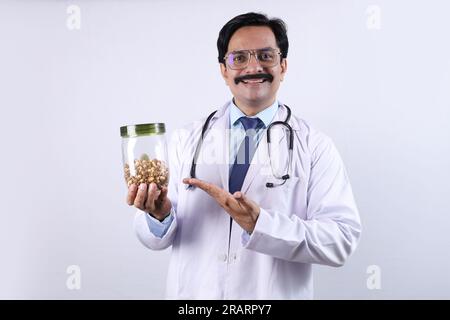 Indischer selbstbewusster Doktor hält ein Glas in der Hand und schlägt vor, frisch und gesund zu essen. Der Arzt steht auf weißem Hintergrund. Stockfoto