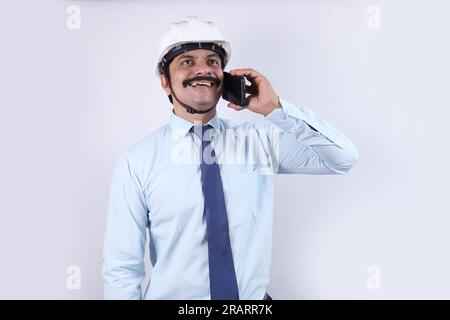 Glücklicher indischer Bauarbeiter, der Ingenieurkonzept für eine bessere Zukunft macht. Der fröhliche Ingenieur trägt einen technischen Helm. Telefonieren. Stockfoto