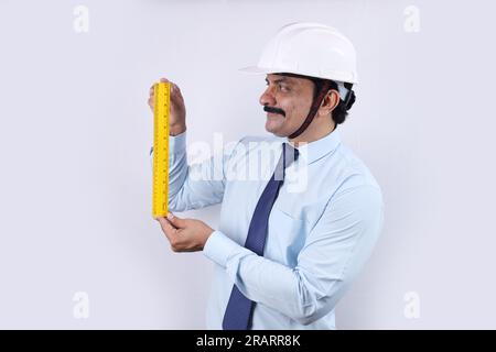 Glücklicher indischer Bauarbeiter, der Ingenieurkonzept für die Zukunft macht. Der fröhliche Ingenieur trägt einen technischen Helm. Messwaage halten. Stockfoto