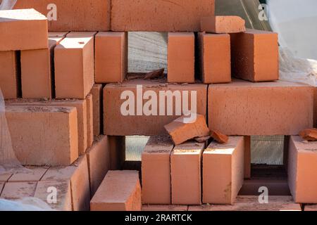 Rote Ziegel in einem Baulager auf der Straße. Baumaterial roter Ziegel mit Löchern. Für den Bau verwendete massive Tonziegel. Konzept der Repa Stockfoto