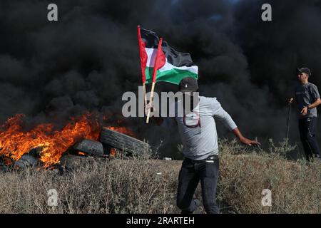 Palästinensische Jugendliche halten während eines Protests am Grenzzaun zu Israel östlich von Gaza-Stadt Flaggen neben brennenden Reifen. Israel hat seine Einsätze im nördlichen Westjordanland, in dem die Stadt Dschenin und das angrenzende Flüchtlingslager untergebracht sind, verstärkt. Gaza-Stadt, Palästina. Stockfoto