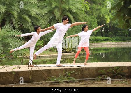 Trainer Training und Unterricht Kinder das Yoga posiert in grüner Umgebung früh morgens im Park, um einen gesunden Lebensstil zu erhalten. Internationaler Yoga-Tag. Stockfoto