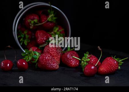 Rote Früchte mit Metalleimer auf einem schwarzen Holztisch, Nahaufnahme, Makrofotografie Stockfoto