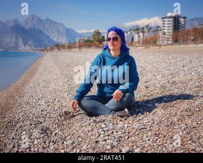 Eine Frau trägt einen hellblauen Hoodie und Jeans in Übergröße. Blauhaarige Frau draußen im Park am Strand von Antalya. Kleidungsmodell, leerer Platz für Text o Design. Stockfoto