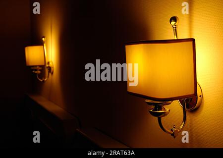 Lampen über dem Bett in einem Hotel erzeugen ein Spiel von Licht, Schatten und warmer Atmosphäre. Stockfoto