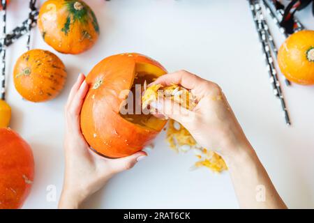 Halloween 31. Oktober. Der Schritt-für-Schritt-Prozess des Kürbisschnitzens. Das Mädchen bekommt Samen vom Kürbis Stockfoto