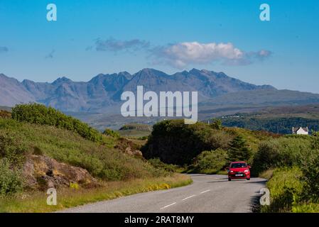 Isle of Skye, Schottland, Vereinigtes Königreich. 5. Juni 2023 Kleines rotes Auto und malerischer Blick auf die Cuillin Hills mit blauem Himmel. Isle of Skye, Vereinigtes Königreich. Stockfoto