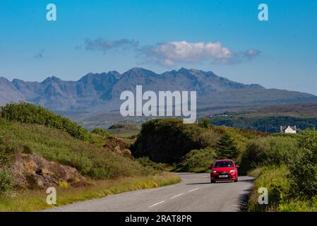 Isle of Skye, Schottland, Vereinigtes Königreich. 5. Juni 2023 Kleines rotes Auto und malerischer Blick auf die Cuillin Hills mit blauem Himmel. Isle of Skye, Vereinigtes Königreich. Stockfoto