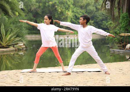 Kinder, die sich sportlich betätigen und Yoga machen, posieren am frühen Morgen im Park in einer grünen, ruhigen Umgebung, um einen gesunden Lebensstil aufrechtzuerhalten. Internationaler Yoga-Tag. Stockfoto