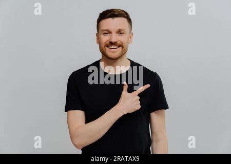 Glücklicher bärtiger Mann in schwarzem Hemd, nach oben zeigend, positiver Ausdruck, Beförderungskonzept. Stockfoto