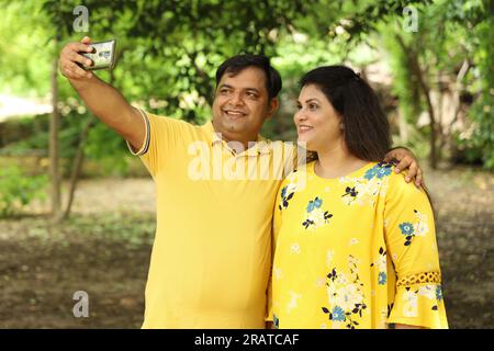 Übergewichtiges indisches Paar, das Selfie im Park macht und ein Handy in der Hand hält. Stockfoto