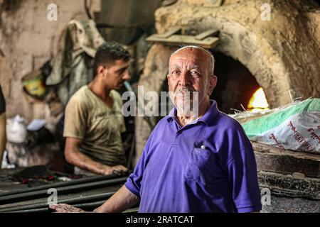 Na'im Sharab, ein 70-jähriger Palästinenser, besitzt den ältesten primitiven Ofen, der vor 130 Jahren von seinen Vorfahren geerbt wurde. Er, seine Kinder und Enkel arbeiten im Ofen der Stadt Gaza. Sharab sagt, dass sie jeden Morgen daran arbeiten, den Ofen vorzubereiten, der mit Holz und verbranntem Öl betrieben wird, das in Geschäften gekauft wurde, die Öle für Autos ersetzen. Mit der Strom- und Gaskrise haben sich einige Menschen daran gewöhnt, Brot, Kaffee und Töpfe in den Ofen zu schicken, wo der größte Anteil an Kochtöpfen während Eid al-Adha hergestellt wird, da Fleisch in großen Mengen verfügbar ist. Palästina. Stockfoto