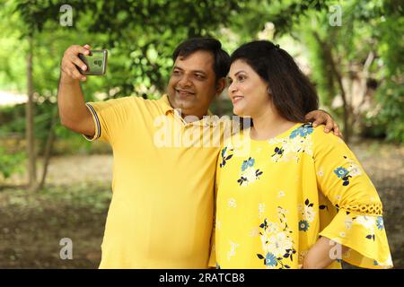 Übergewichtiges indisches Paar, das Selfie im Park macht und ein Handy in der Hand hält. Stockfoto