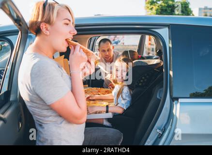 Ein positiv lächelndes Mädchen im Kindersitz, während der Familienausflug mit der Bremse aufgehört hat, gerade gekochte italienische Pizza zu essen. Glückliche Familienmomente, Kindheit, Fast Food Stockfoto