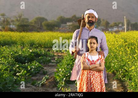 Wunderschönes dramatisches Porträt eines wütenden indischen Bauern und einer Tochter, die auf dem Senffeld mit Kurta-Pyjama und Schaufel in der Hand stand. Stockfoto