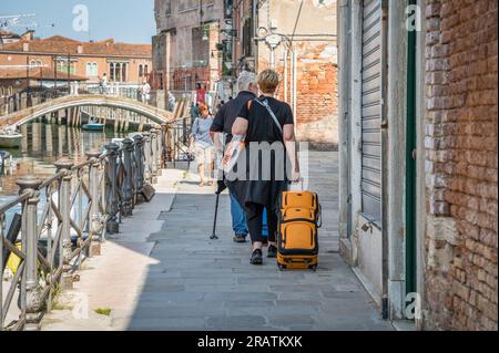 Eine nicht identifizierbare Touristin mit einem Gepäckwagen, die in der Nähe eines Wasserkanals in Venedig, Italien, läuft. Stockfoto