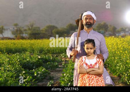 Wunderschönes dramatisches Porträt eines wütenden indischen Bauern und einer Tochter, die auf dem Senffeld mit Kurta-Pyjama und Schaufel in der Hand stand. Stockfoto